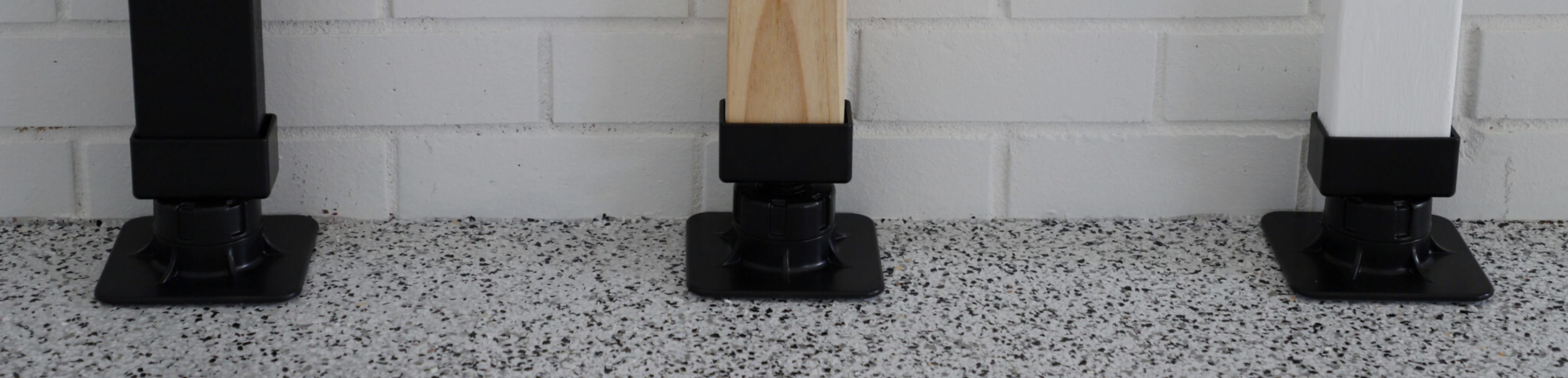 Three wooden posts with black bases on a speckled floor against a white tiled wall.